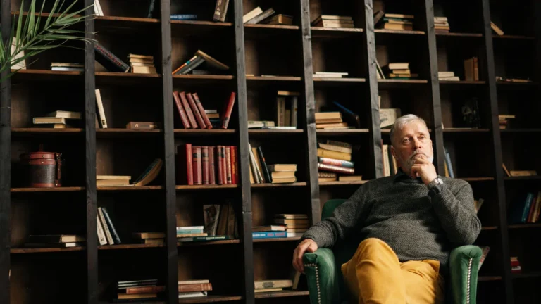 Thoughtful man sitting in a library surrounded by tall bookshelves