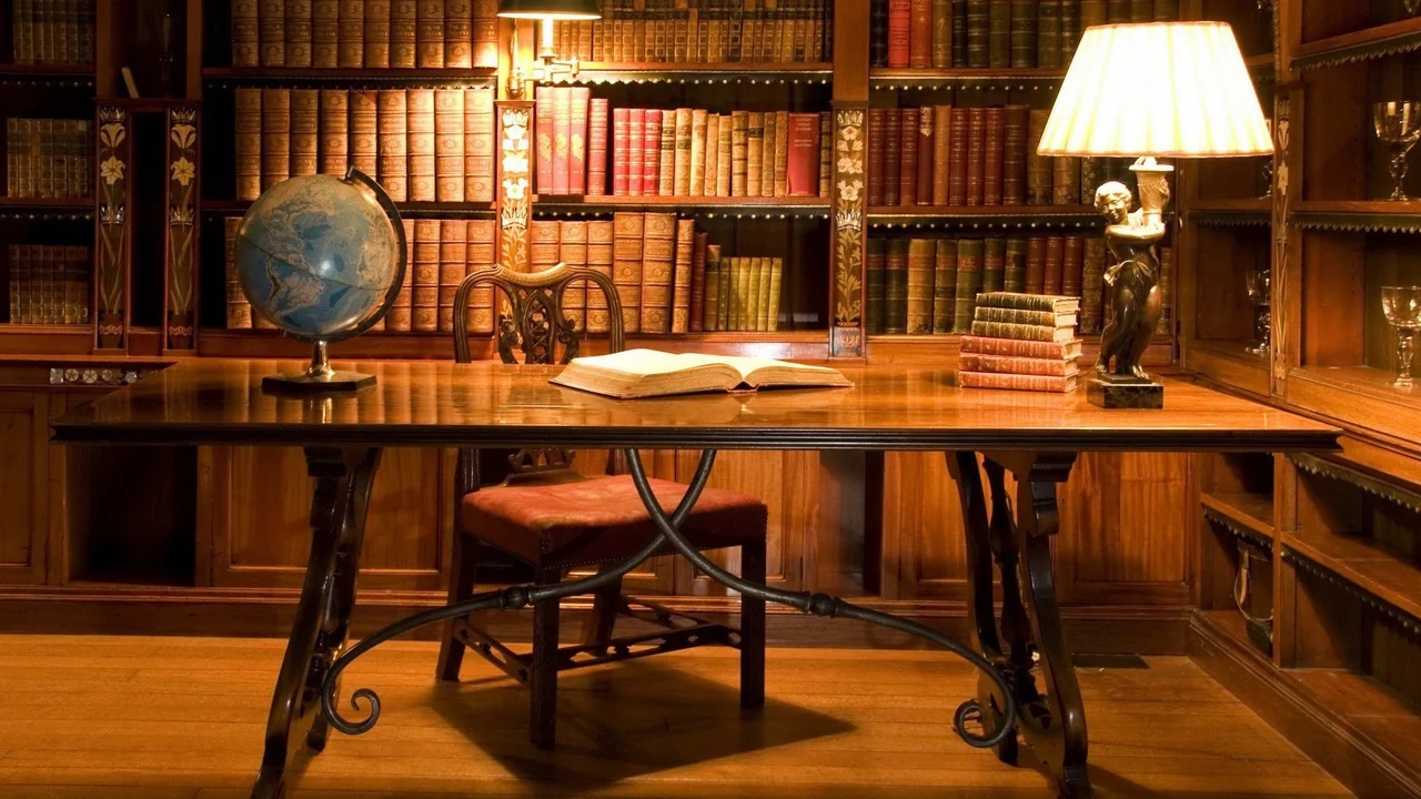 Warm wooden library study desk with a globe, lamp, and open book